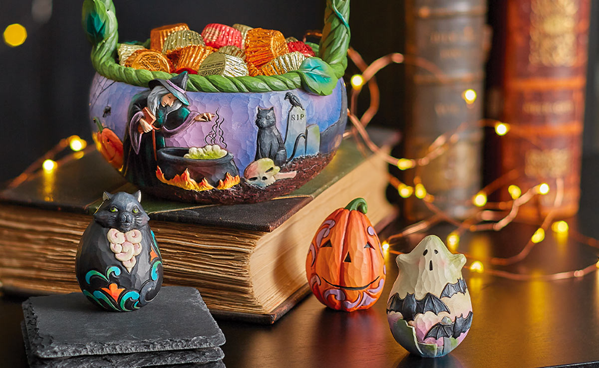 A Heartwood Creek Halloween basket statue filled with candy atop a stock of books accented by mini Halloween figurines.